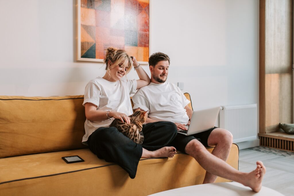 A couple relaxing on a sofa with a laptop and their cat