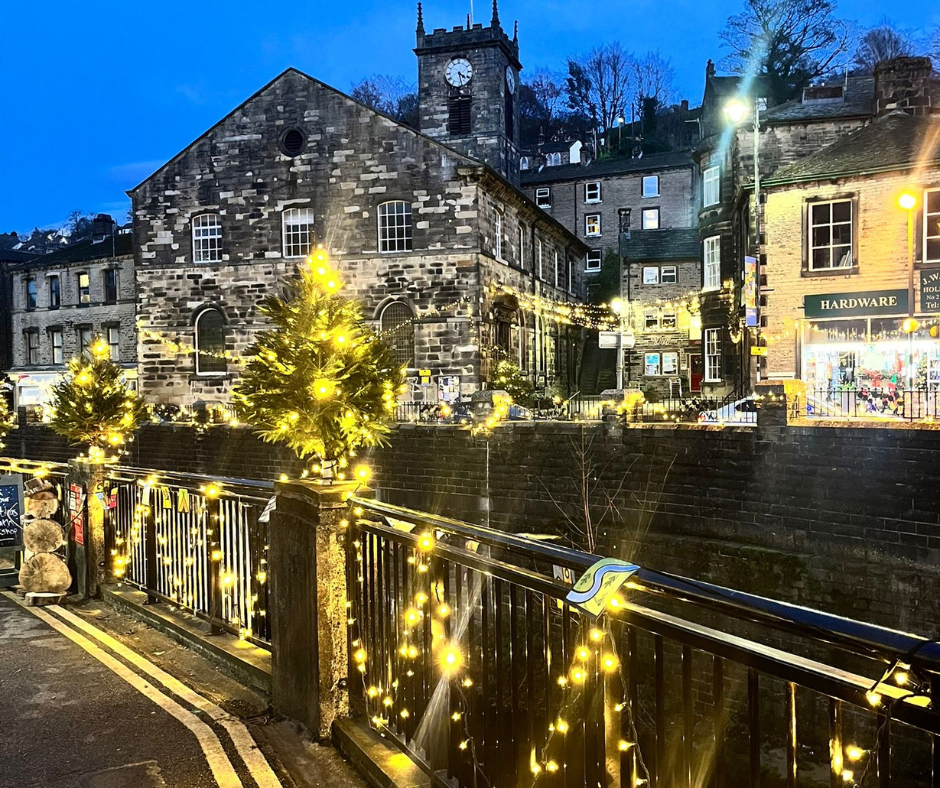 A Yorkshire town centre at dusk with Christmas lights and lit trees along a bridge