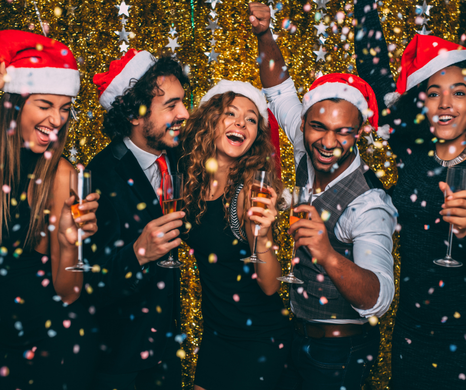 A group of friends in Santa hats celebrating with drinks and confetti
