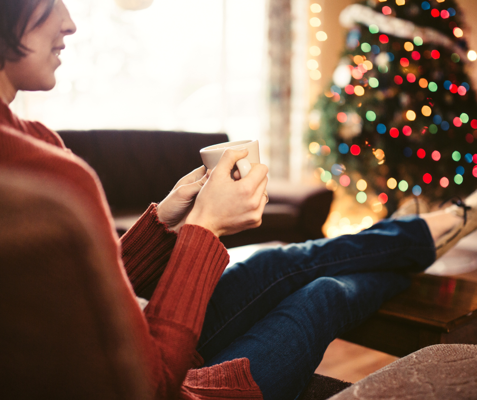 A woman relaxing with a hot drink beside a Christmas tree