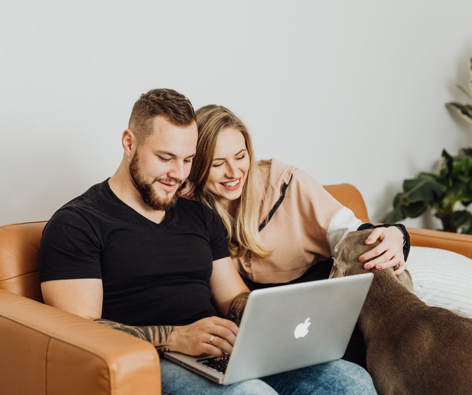 A couple sitting on a sofa looking at a laptop together with their dog