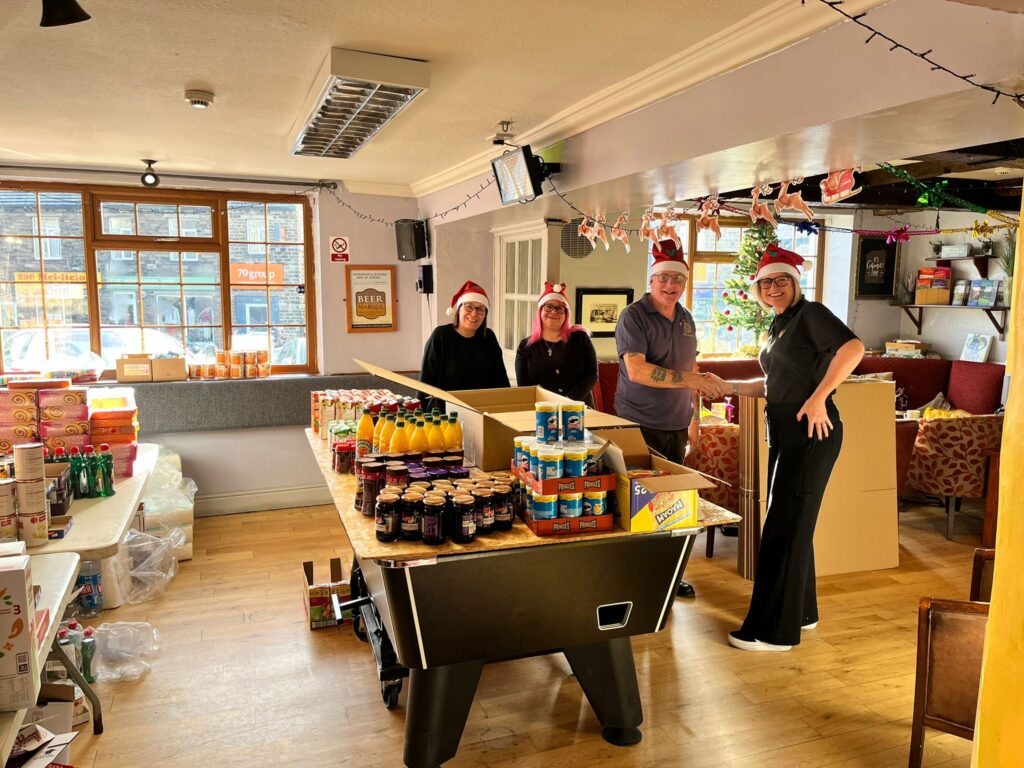 Four people in Santa hats with boxes of donated food in a village pub