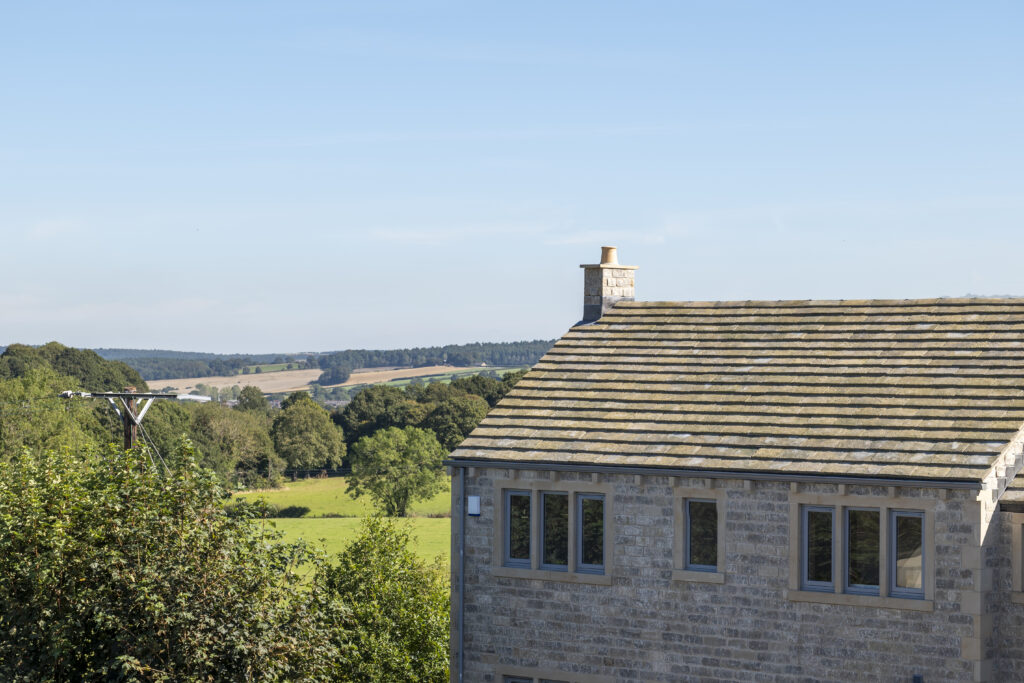 The roof and chimney of a new stone home with open countryside beyond