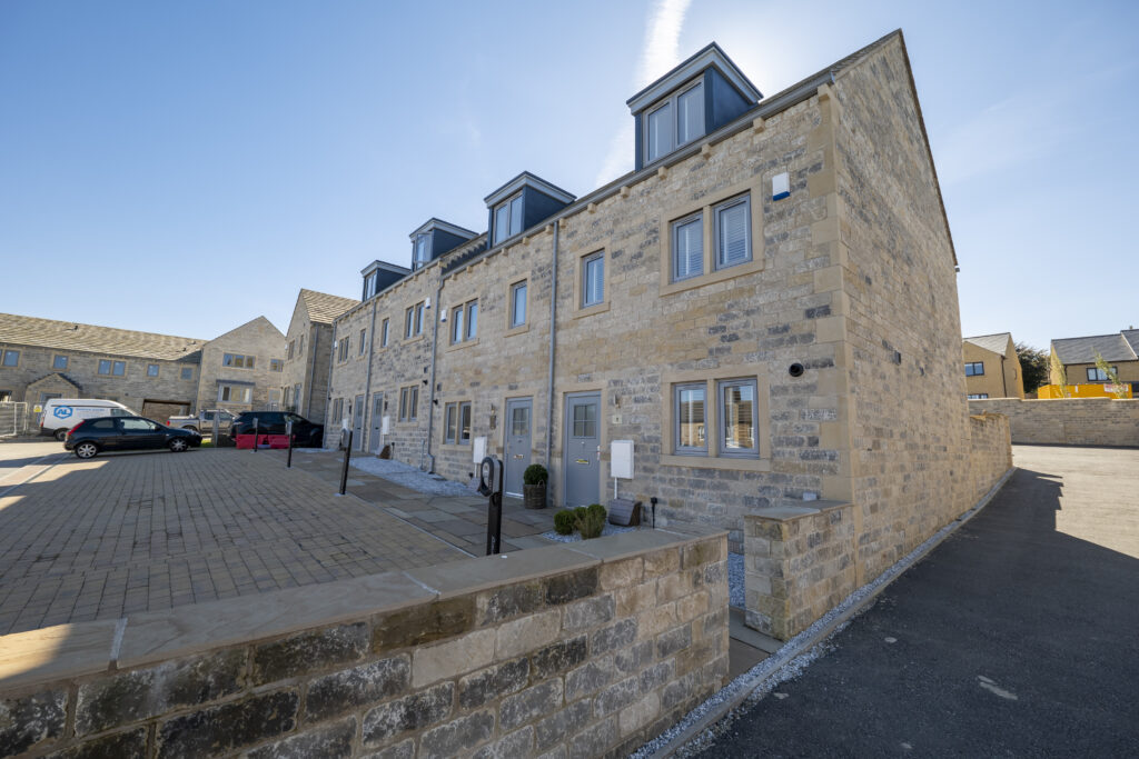 A terrace of new stone townhouses with dormer windows and parking in front