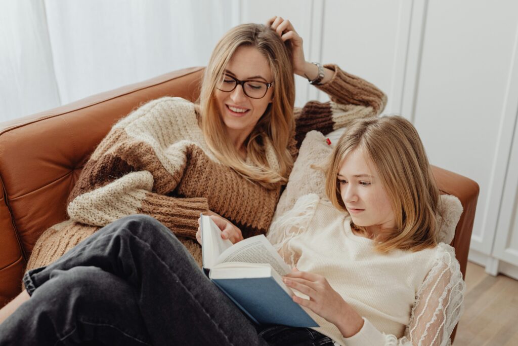 A woman and a teenager reading a book together on a sofa