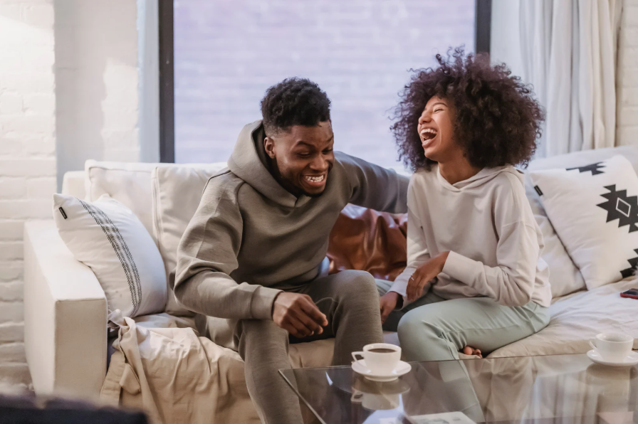 A couple laughing together on a sofa with cups of coffee