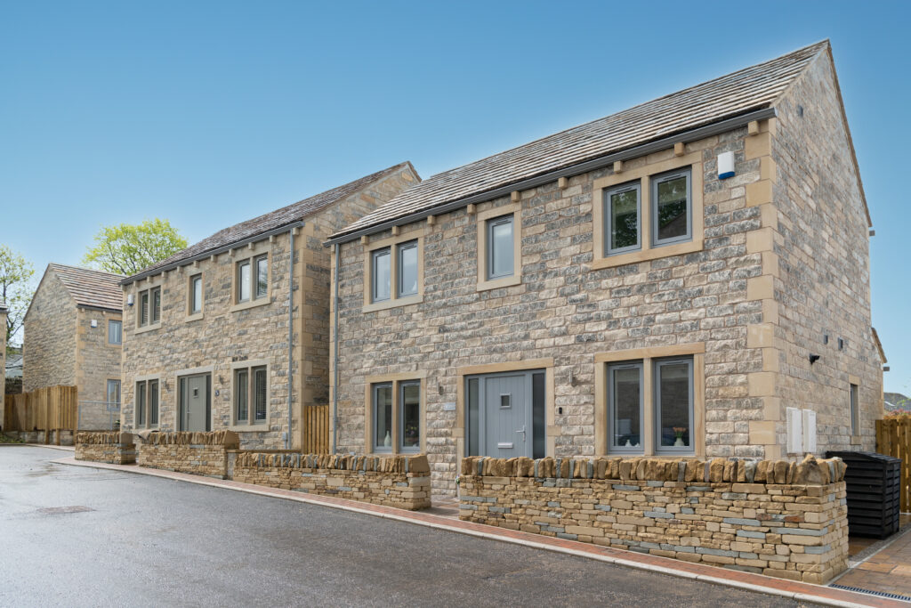 A pair of new stone homes behind a dry stone wall