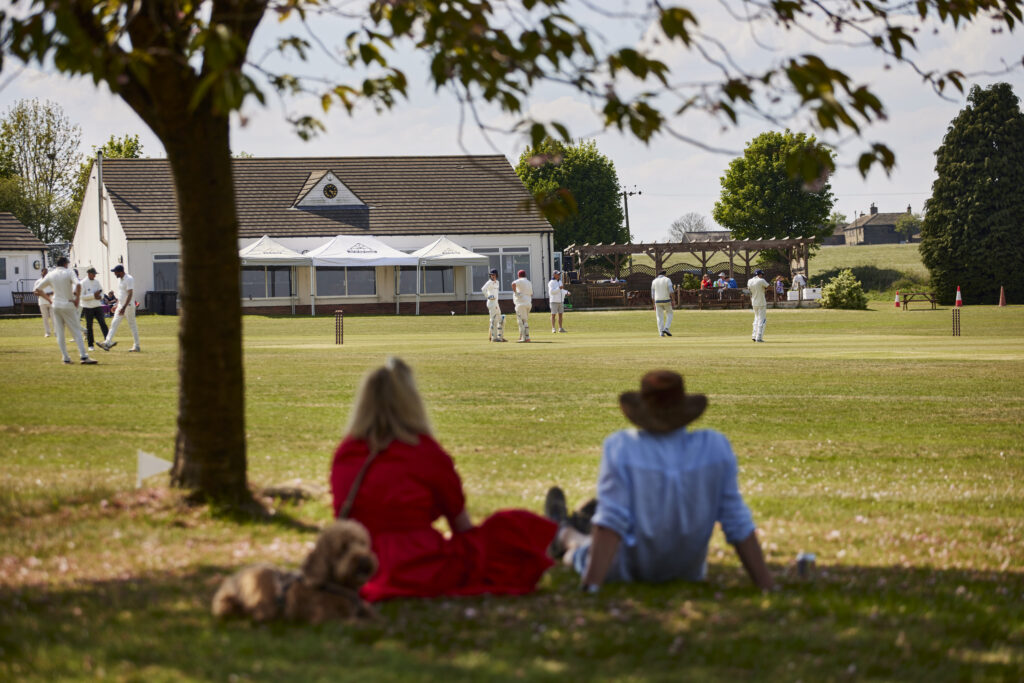 People watching a village cricket match from the shade of a tree