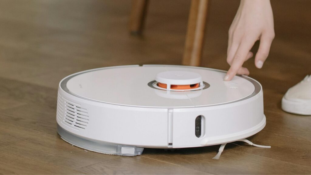 A hand switching on a robot vacuum cleaner on a wooden floor
