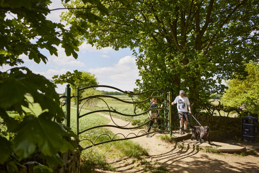 A couple walking their dog through a decorative metal gate onto a field path